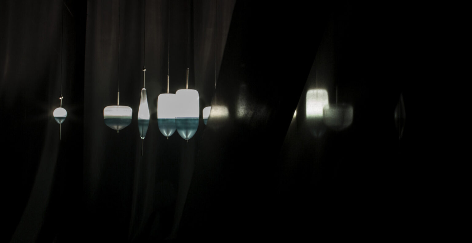 MOVING HORIZON, WonderGlass. Installation by Nao Tamura. | Milan 2013, as built. An early FLOW[T], the water darker and the shape not yet final. Unlit, it was already right; lit, the top burned out. The final form came from repeating this.